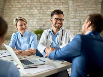 Happy doctor shaking hands with a businessman on a meeting in th Startseite group healthcare workers greeting financial advisor meeting office focus is young doctor scaled Versicherungspapa