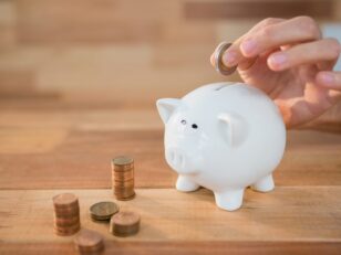 Hand inserting coin in piggy bank Asbestprüfungen verteuern Wohngebäudeversicherungen hand inserting coin piggy bank scaled Versicherungspapa
