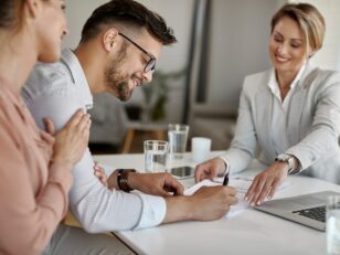 Young man signing a contract while being with his wife on a meet Assistenzsysteme könnten jeden zehnten Autounfall verhindern happy man his wife having meeting with financial advisor signing agreement office scaled Versicherungspapa