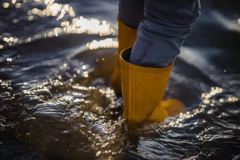 Wehrlos gegen Extremwetter person blue denim jeans yellow boots standing water 1 scaled Versicherungspapa