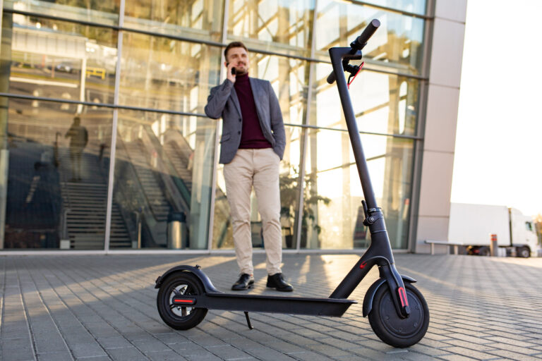 Mofas und E-Scooter sollen Dauerkennzeichen erhalten young handsome man with e scooter standing sidewalk near airport sunset talking smartphone 1 scaled Versicherungspapa